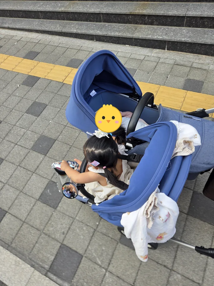 앞보기 좌석의 첫째와 배시넷에 누운 둘째가 함께 탄 연년생 유모차(둘째 얼굴은 병아리 그림으로 가림)