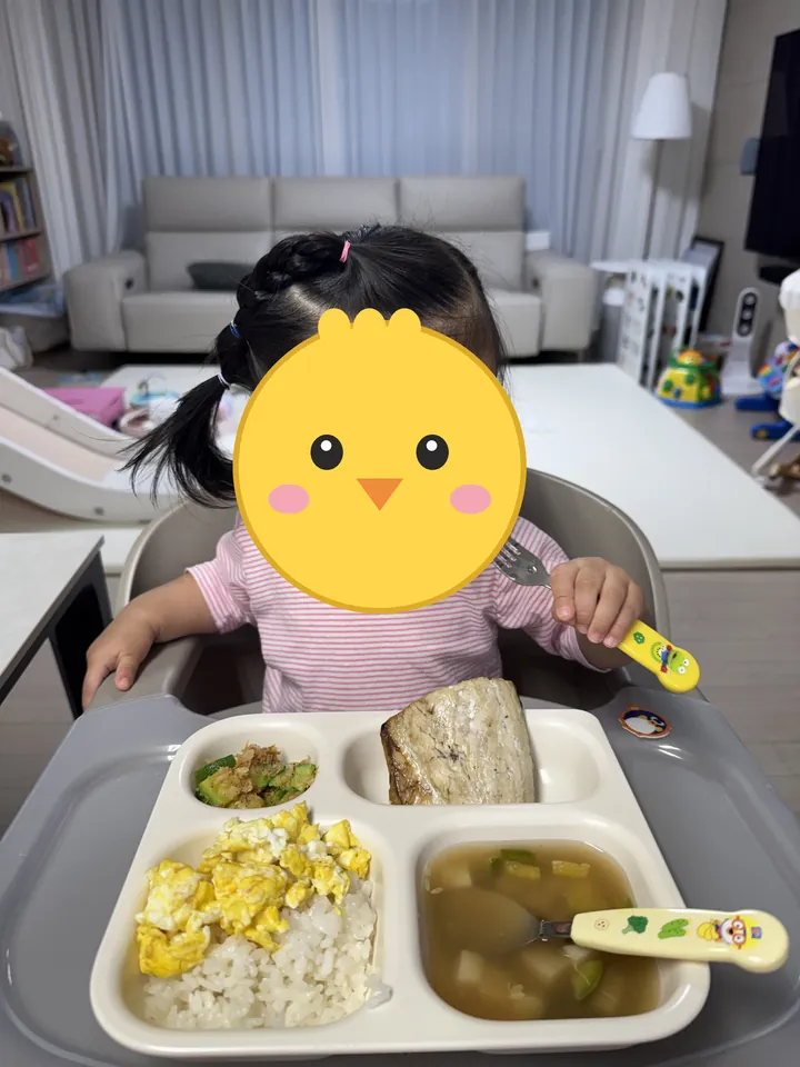 아기 의자에 앉아 포크로 식판 밥을 먹는 첫째(얼굴은 병아리 그림으로 가림)